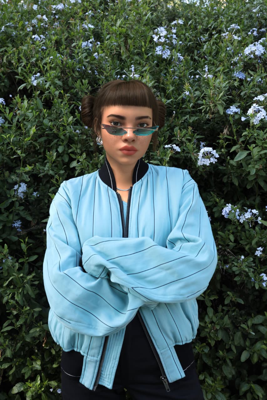 Virtual influencer Lil Miquela with brown bob hairstyle and space buns in light blue bomber jacket and turquoise sunglasses posing against flowering hedge backdrop